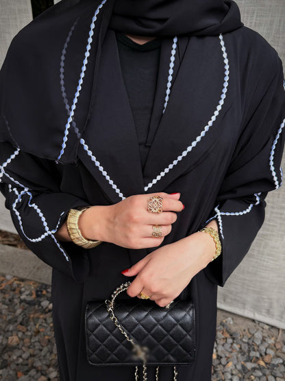 Close-up of white embroidered trim on the black abaya lapels and matching hijab. 5