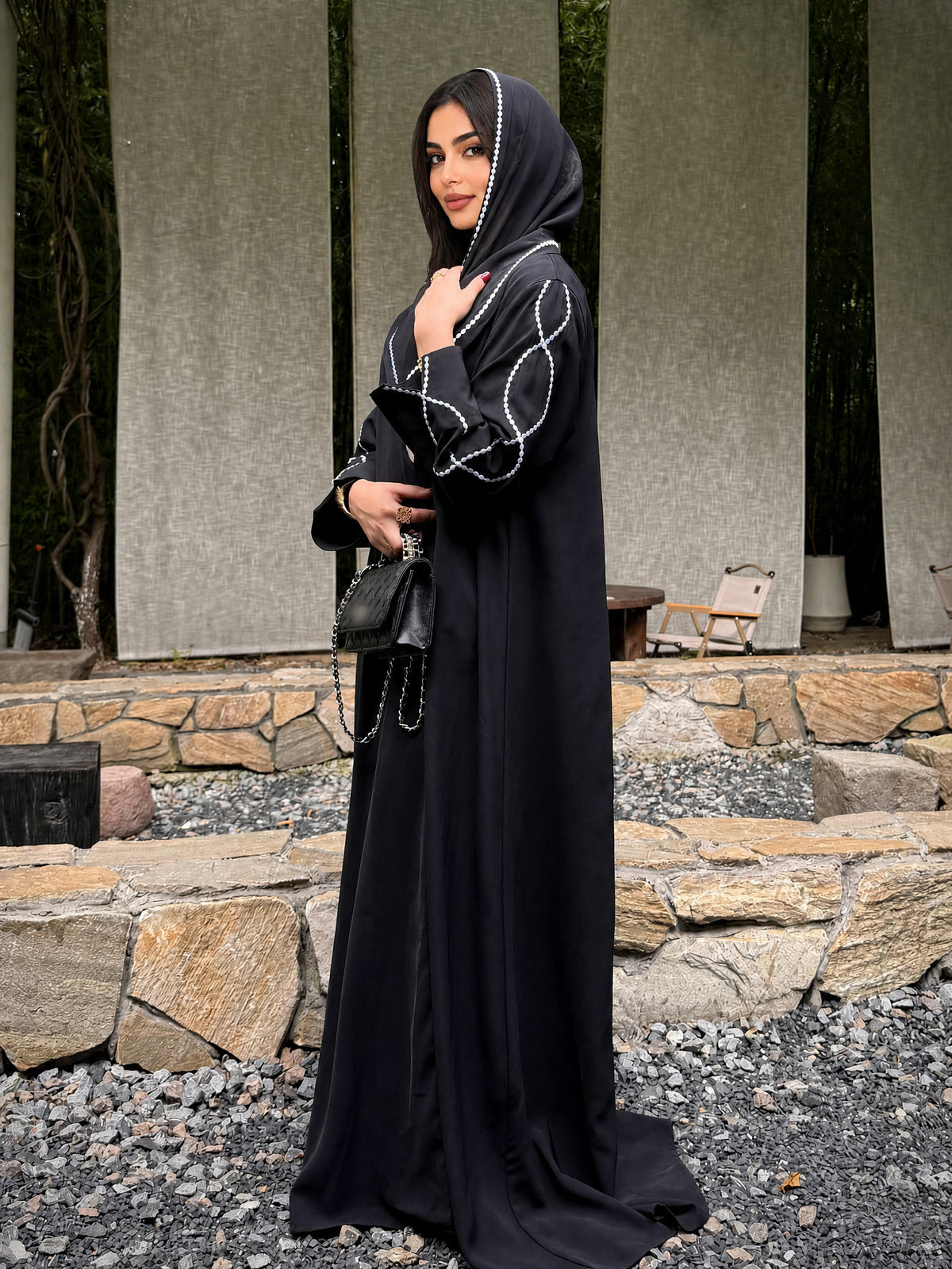 Full-length side view of the black embroidered abaya and matching hijab with white edging.