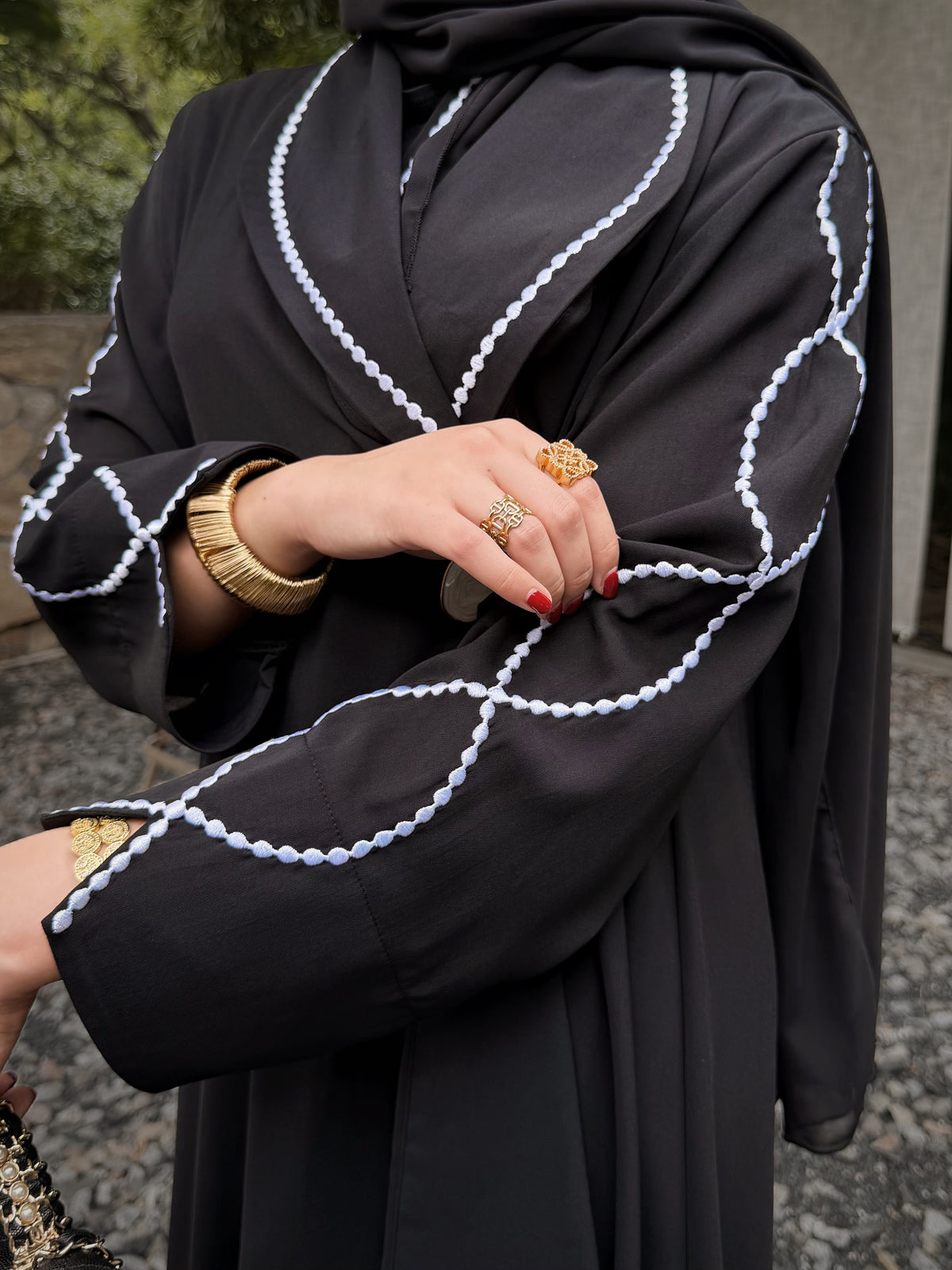 Detail of white loop embroidery across the black abaya sleeve and cuff.
