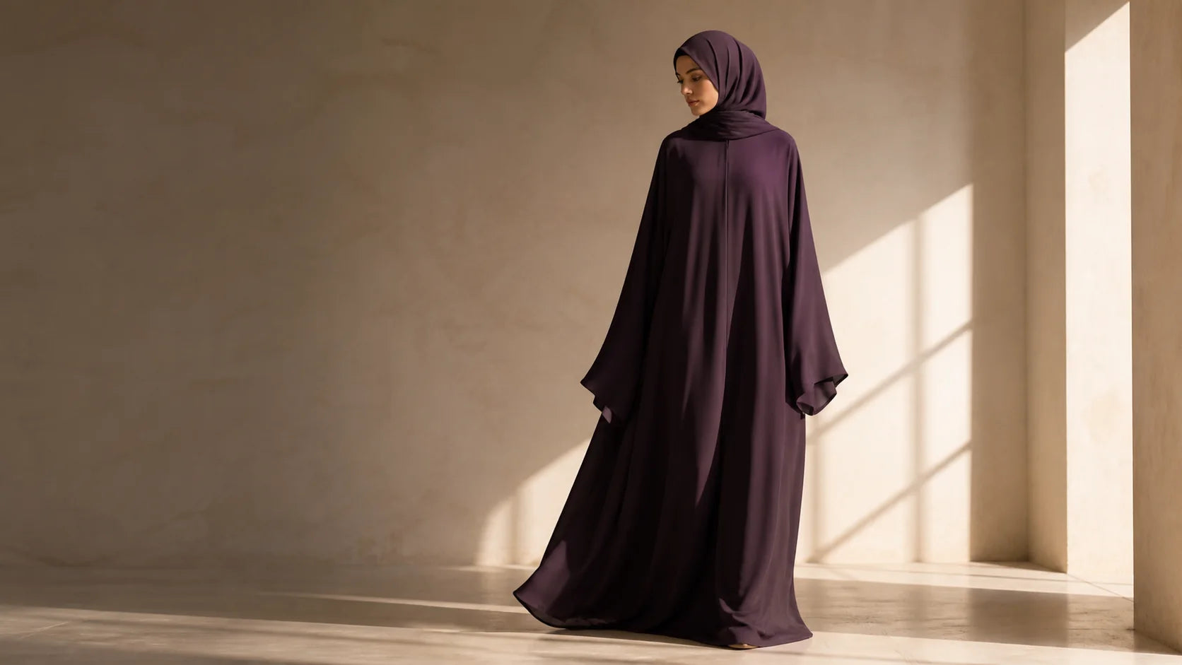 Woman in a deep plum flowing abaya standing in warm architectural light