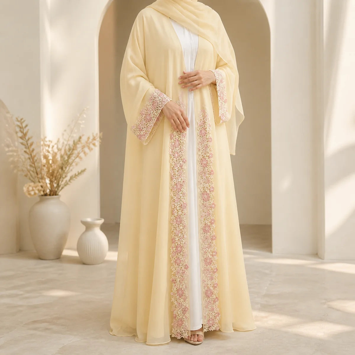 Pale yellow open abaya with pink lace detailing in a softly lit arched interior